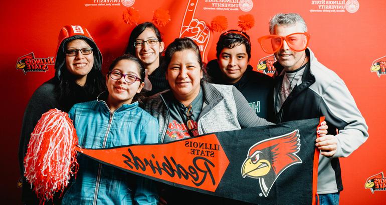 A family wears goofy props and holds an ISU banner